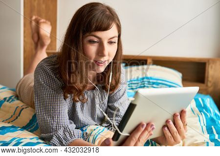 Smiling Young Woman Lying On Bed And Watching Show Or Sitcom On Digital Tablet