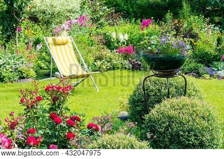 A Beautiful Blooming Flower Garden With Yellow Deck Chair On A Green Lawn In Summer