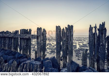 View Of The Wadden Sea During Sunset, At Low Tide. A Colorful Dramatic Sky. Wooden Posts As A Silhou