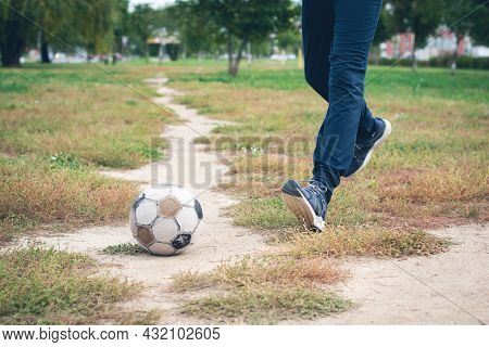 Old Soccer Ball With Teenager Feet On The Football Field. Selective Focus.