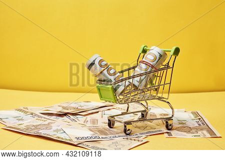 Buying Us Dollars In Uzbekistan. Us Dollars Roll In Shopping Trolley And Pile Of Uzbek Sums. Uzbek M