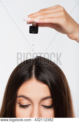 Cropped View Of Young Woman With Shiny Hair Applying Treatment Oil On Top Of Head Isolated On Grey