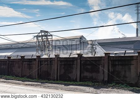 Steel Manufacturing Facility On A Sunny Day, Long Tall Stucco Security Wall, Horizontal Aspect