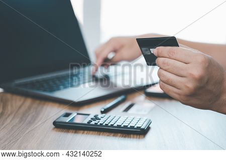 A Man Hold Credit Card In Hand  Enter Card Number On Laptop Computer And Calculator On Wood Table Fo