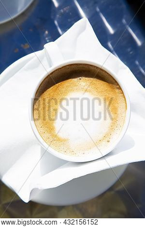 Top View To A Hot Fresh Cup Of Capuccino In Bright Sunlight. White Mug Of Hot Coffee With Milk On Wh