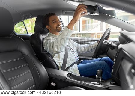 transport, driving and people concept - happy smiling indian man or driver adjusting mirror in car