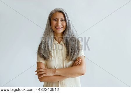 Portrait Of Smiling Asian Woman With Hoary Hair And Crossed Arms On Grey Background