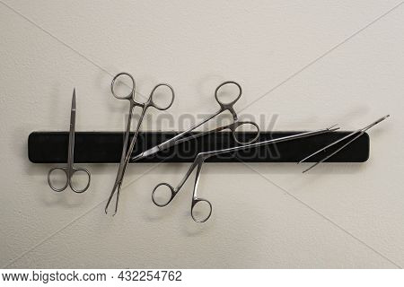 Metal Surgical Instruments On A Magnetic Bar On A Clinic Wall.