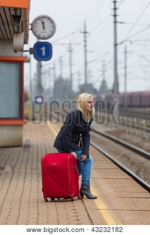 una giovane donna con i bagagli in attesa sulla piattaforma di una stazione per i treni. ritardo treno