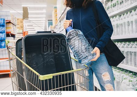 Woman Shopping Bottle Of Water In Supermarket For Stocking Up Supplies During Covid-19 Pandimic Outb
