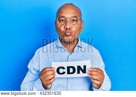 Middle age latin man holding cdn message paper looking at the camera blowing a kiss being lovely and sexy. love expression. 