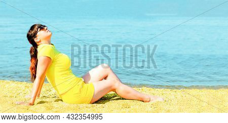 Young Beautiful Woman In Yellow Shorts And A T-shirt Sits On The Seashore And Looks Up. Wonderful Su