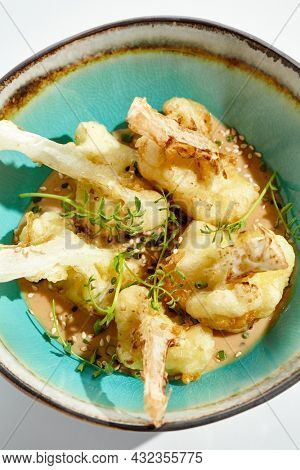 Fried tempura cauliflower with peanut sauce in bowl. Vegeterian hot dish - florets cabbages roasted  in batter on white background. Veggie menu for asian restaurant. Hot vegan appetizers plant based
