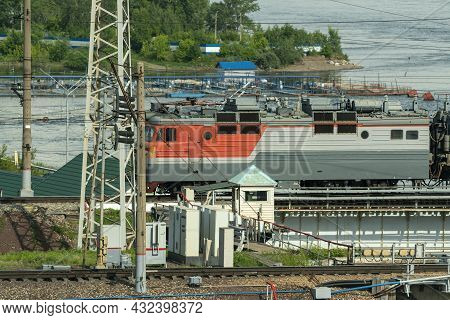 An Electric Locomotive On The Railroad Tracks Near The River Bank.
