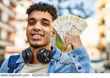 Hispanic young man holding 100 danish krone baknotes at the street