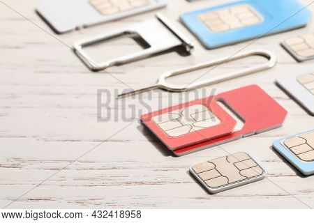 Different Sim Cards, Ejector And Tray On White Wooden Background, Closeup