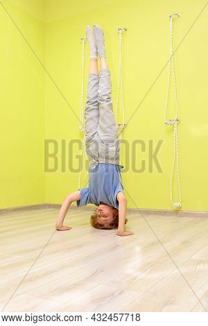 The Boy Stands In His Arms In The Gym Against The Wall. The Child Is Doing Yoga, Doing A Headstand.