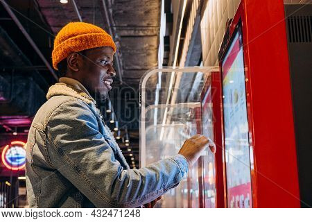 Positive African-american Guy In Orange Knitted Hat With Wireless Earphones Orders Food Through Self