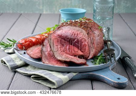 Modern style traditional barbecue haunch of venison sliced and as piece served with tomatoes and herbs as close-up on a Nordic design plate