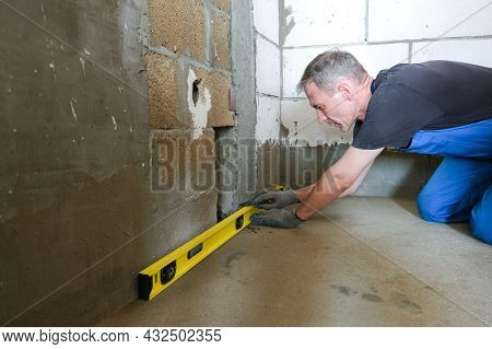 A Male Worker Checks The Evenness Of The Floor And Walls Before Repairing, Using A Building Level. T