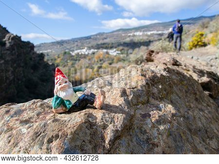 Gnome Lying On A Rock And In The Background Hikers And Villages Of La Taha In The Alpujarra