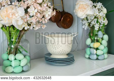 Enameled White Colander, Plates, Bouquet Of Flowers In Vase And Easter Eggs On Kitchen Table. Front 