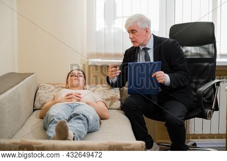 Caucasian Woman Lies On A Couch At A Reception With A Psychotherapist. An Elderly Man Works As A Psy