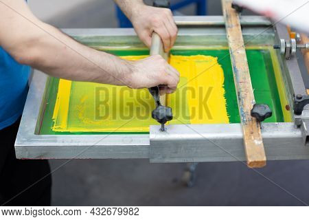 Serigraphy Silk Screen Print Process At Clothes Factory. Frame, Squeegee And Plastisol Color Paints.
