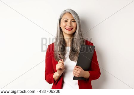 Successful Asian Lady Boss In Red Blazer, Holding Clipboard With Documens And Pen, Working And Looki