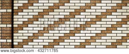 The Wall Of The Building Is Lined With Facing Bricks Or Tiles. Beige And White Bricks Alternate And 