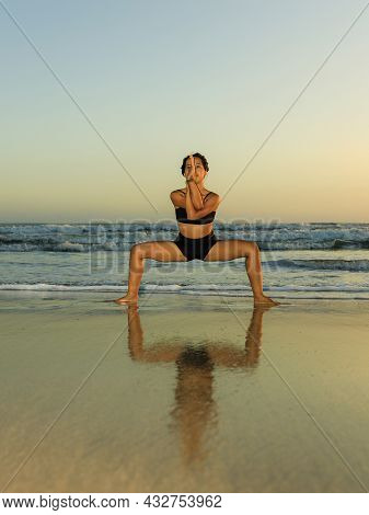 Beach Yoga Practice. Young Woman Practicing Utkata Konasana, Goddess Pose. Hands In Eagle Pose. Open