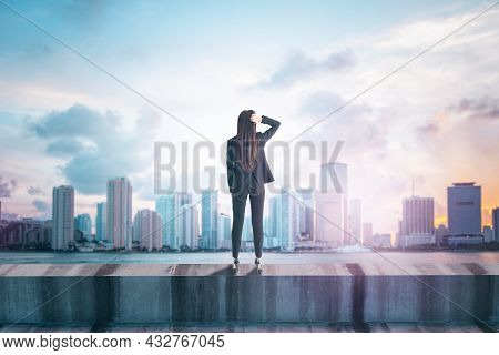 Back View Of Young Female Standing On Concrete Edge Of Building On City Background With Mock Up Plac
