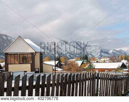 Russian Village Chemal In The Snow. Houses Covered With Snow Against The Background Of The Altai Mou