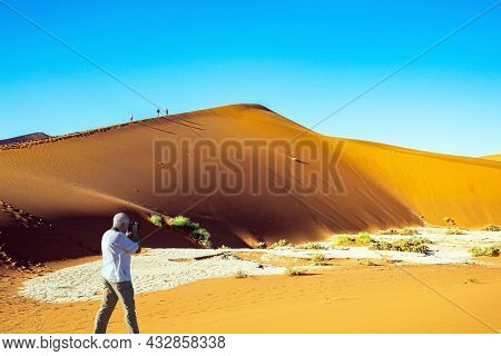 Man takes pictures of a magnificent landscape. The Namib Naukluft Park. Namibia. Africa. The clay plateau Sossusflei 