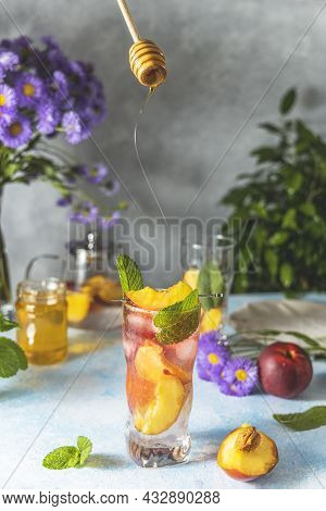 Woman Hand Perfused Honey On Peach Infused Water, Cocktail, Lemonade Or Tea. Summer Iced Cold Drink 