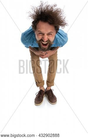 young casual man leaning forward and laughing at the camera on white background