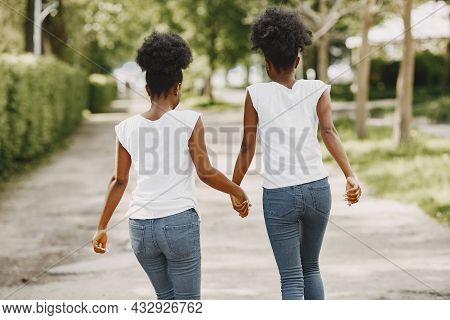 Twin Afro-american Sisters Holding Hands And Walking In A Park