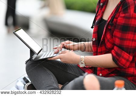 Cropped Image Of A Young Woman While Using A Tablet Computer With A Stylus Pen In An Urban Park.