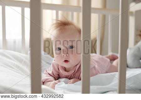 Cute infant girl in pink clothes looking at you while crowling in her cradle