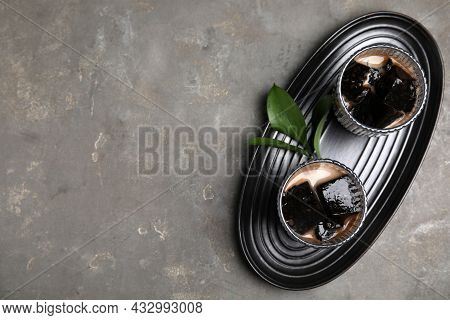 Glasses Of Milk With Grass Jelly And Green Leaves On Grey Table, Top View. Space For Text