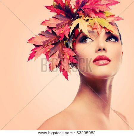 Autumn Woman Fashion Portrait. Beauty Autumn Girl with colorful yellow and red Leaves on her Head. Hairstyle and Makeup. Fall. Glamour Fashion Model closeup 