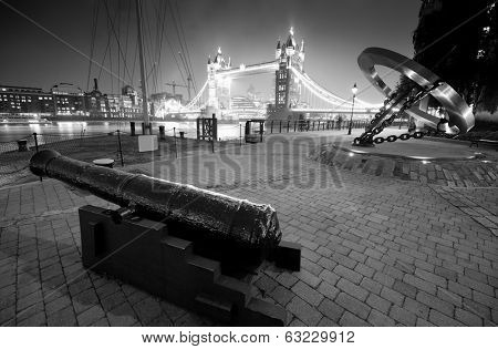 Cannon and Tower Bridge at night at St. Katherine Dock in London.