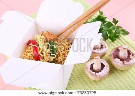 Chinese noodles and sticks in takeaway box on green napkin on pink background