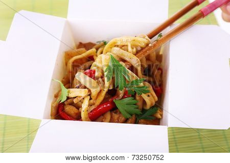 Fried noodles in takeaway box on mat background