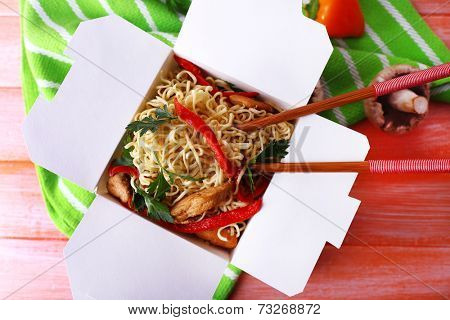 Chinese noodles and sticks in takeaway box on green napkin on pink background