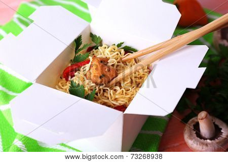 Chinese noodles and sticks in takeaway box on green napkin on pink background