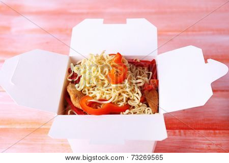 Chinese noodles with meat and pepper in takeaway box on pink background