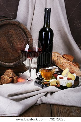 Supper consisting of Camembert and Brie cheese, honey, wine and grapes on napkin and wine barrel on curtain background