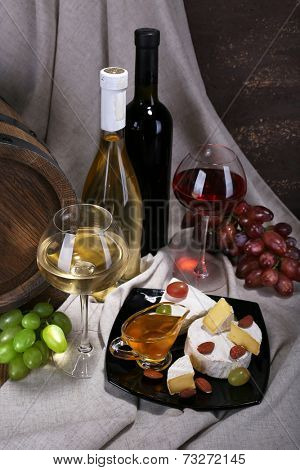 Supper consisting of Camembert and Brie cheese, honey, wine and grapes on napkin and wine barrel on curtain background