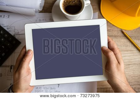 Contractor holding tablet pc above work desk 